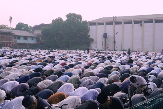 Large group of people gathered outdoors for prayer at dusk. Community, faith, and tradition are highlighted.